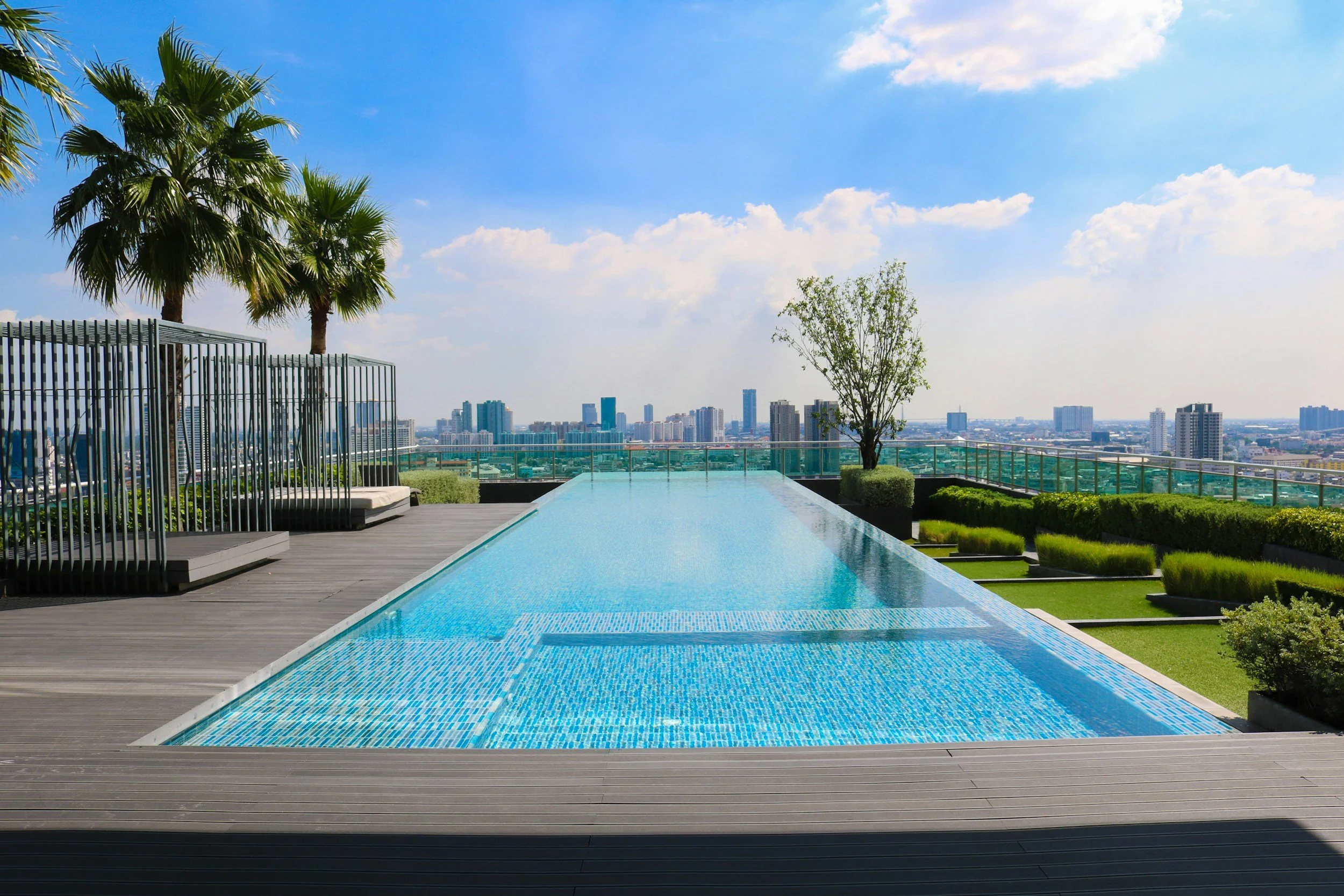 Rooftop infinity pool overlooking a city skyline with trees and lounge area.