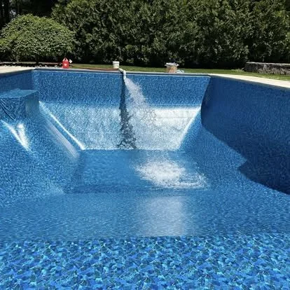 Empty backyard swimming pool with cascading waterfall feature and surrounding greenery.