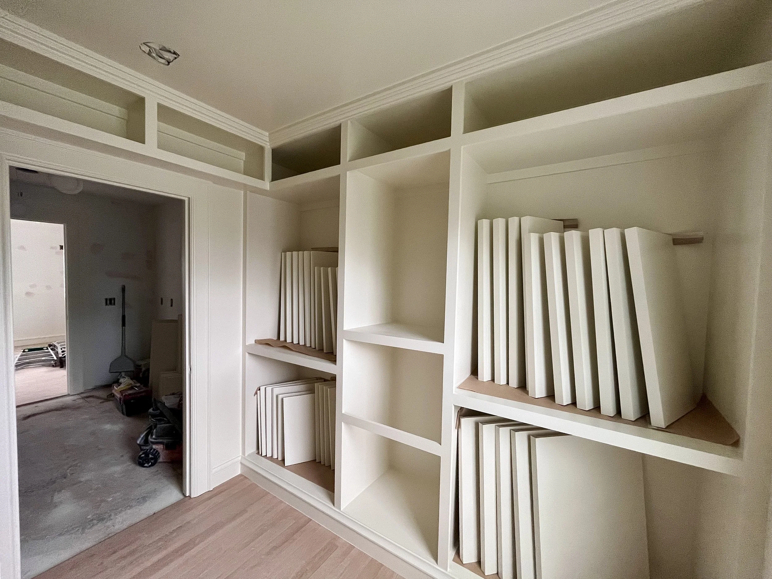 White built-in bookshelf with several empty shelves and some white foam back panels stored against the shelves, situated in a room under construction or renovation.