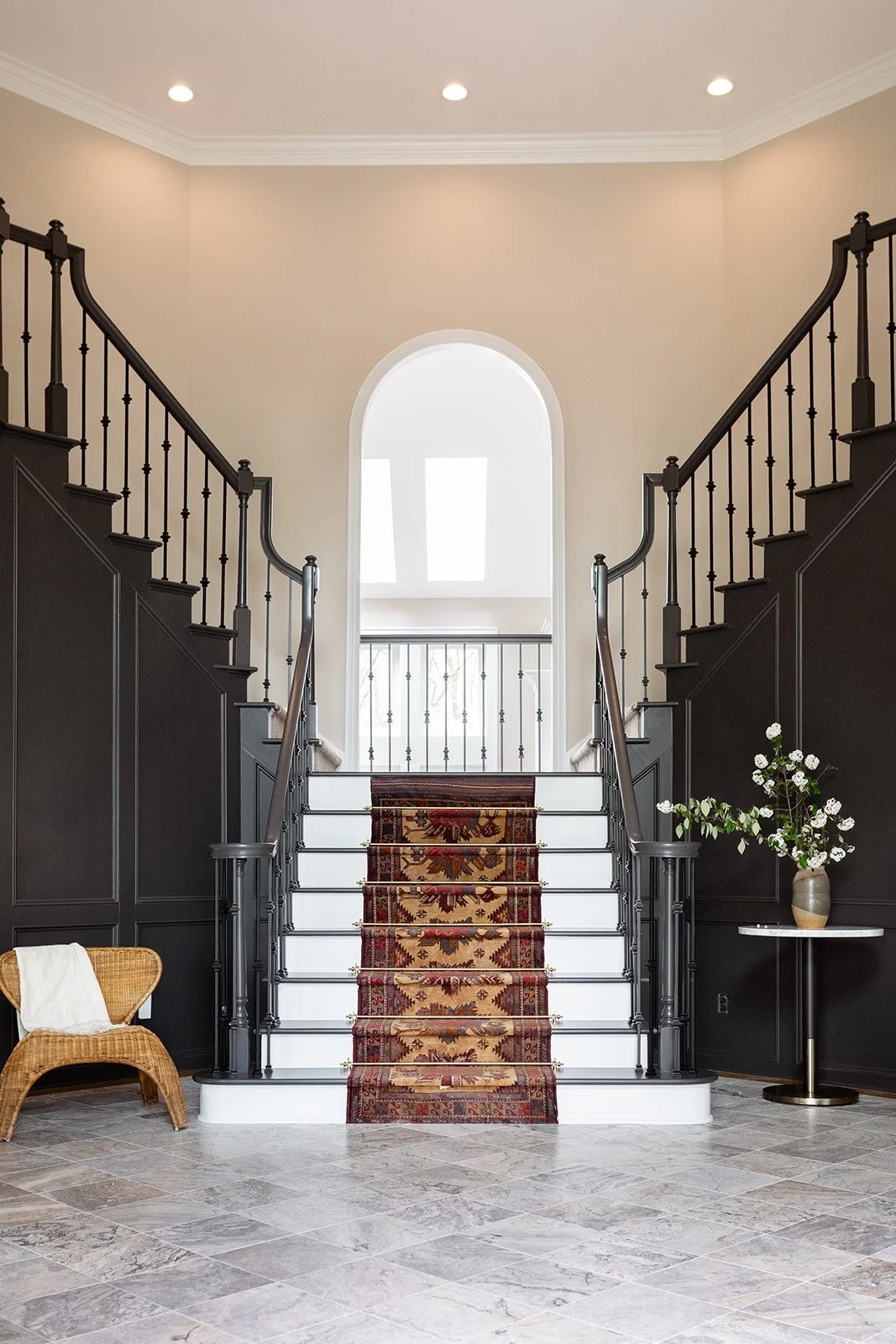Interior view of a staircase with dark wood paneling, a patterned runner, and a vase with flowers beside the stairs, in a well-lit room with skylights.