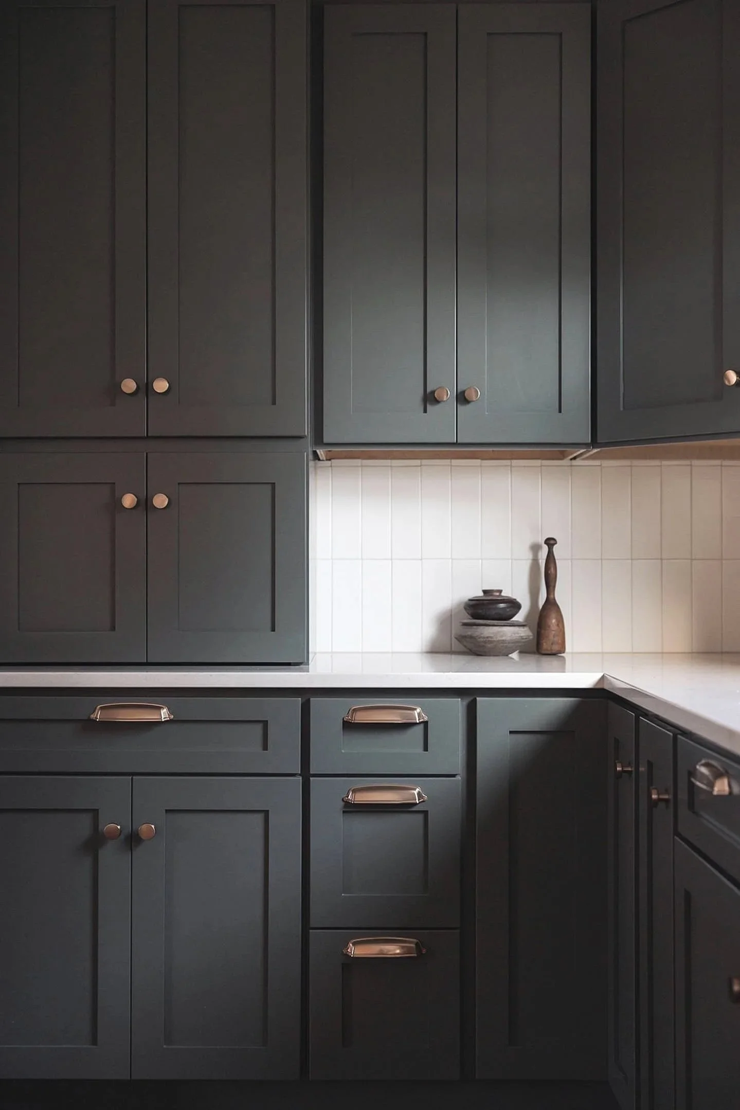Kitchen with dark cabinets, white countertops, and decorative vases on the counter.