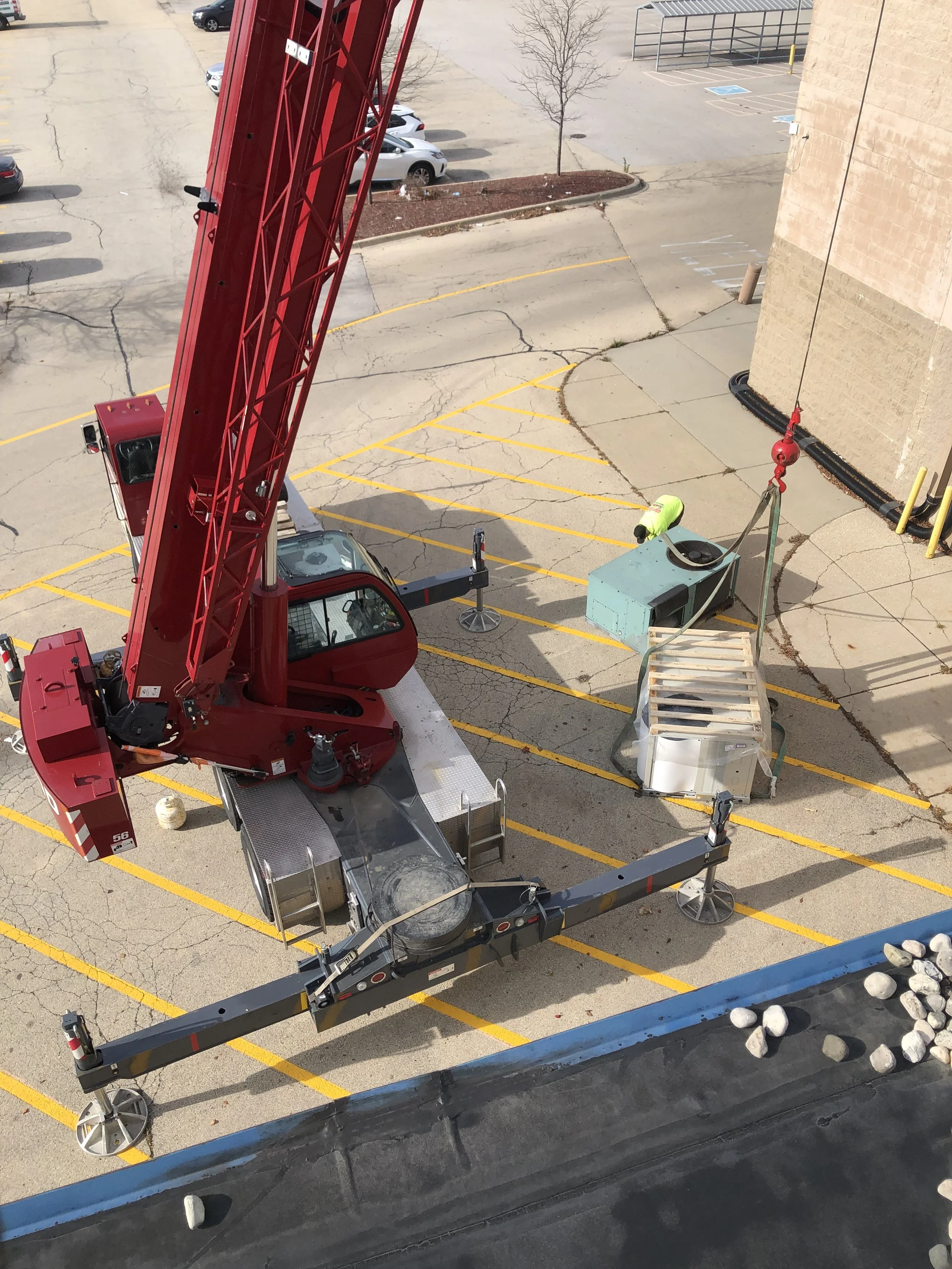 View of a red crane on a construction site, with parking lot and a person in a yellow jacket working near construction equipment.