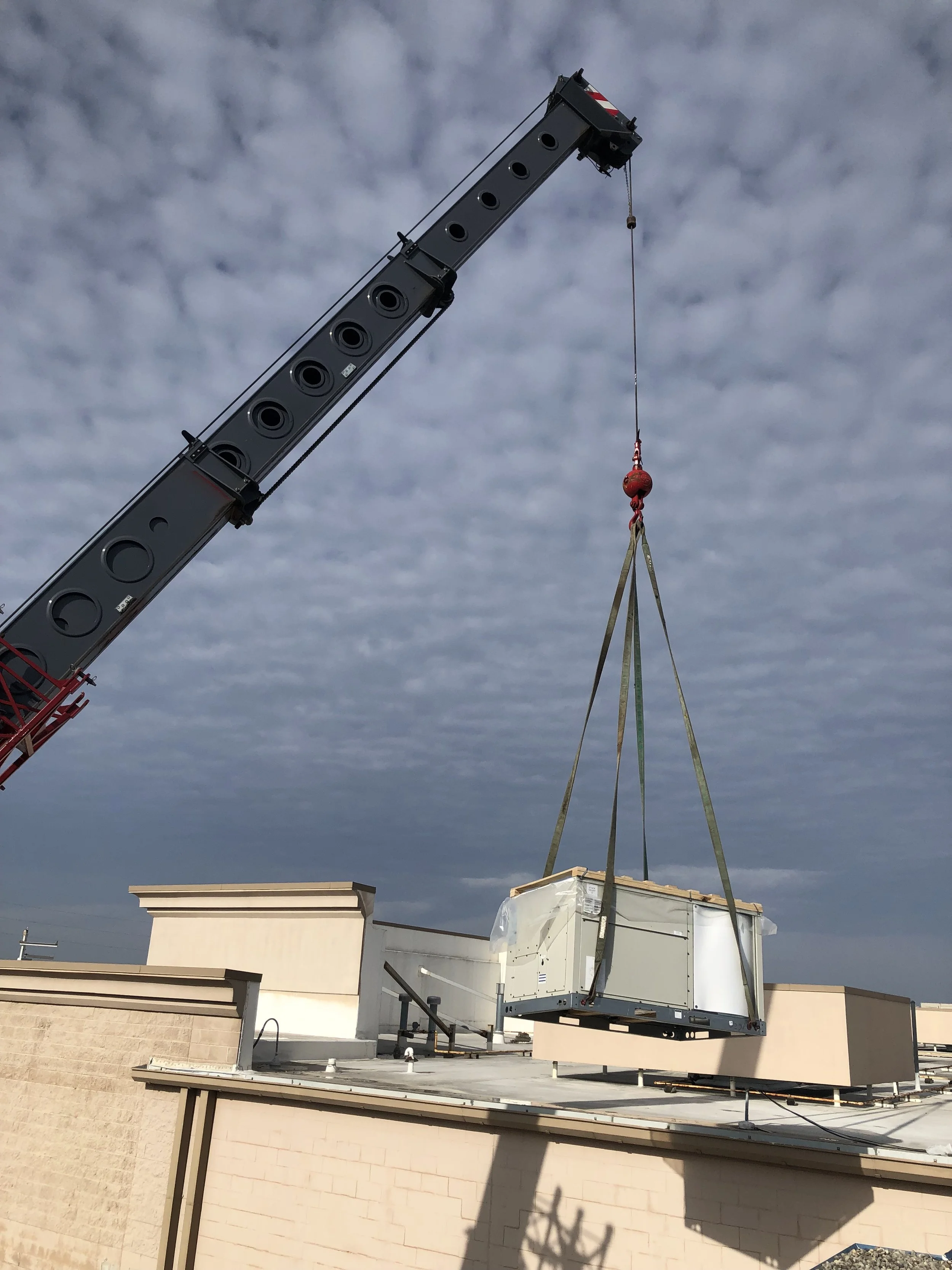 A crane lifting a large HVAC unit onto a rooftop against a cloudy sky.