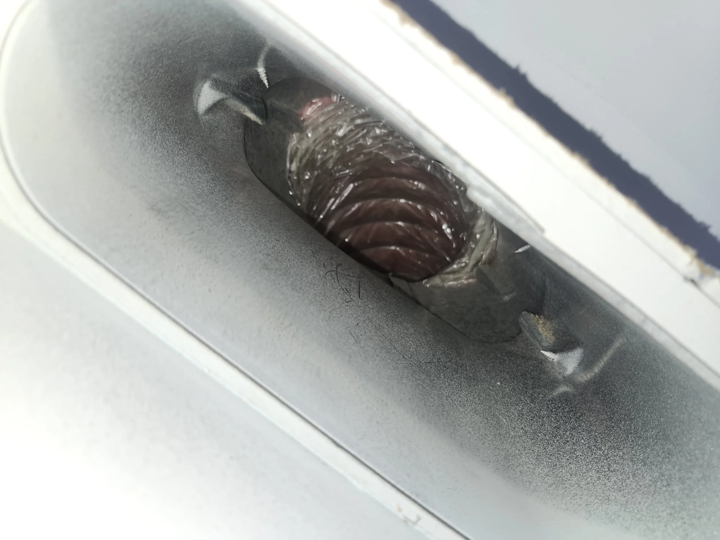 Close-up of a metallic slot with a damaged spiraled plastic or metal component inside, part of a larger machine or appliance.