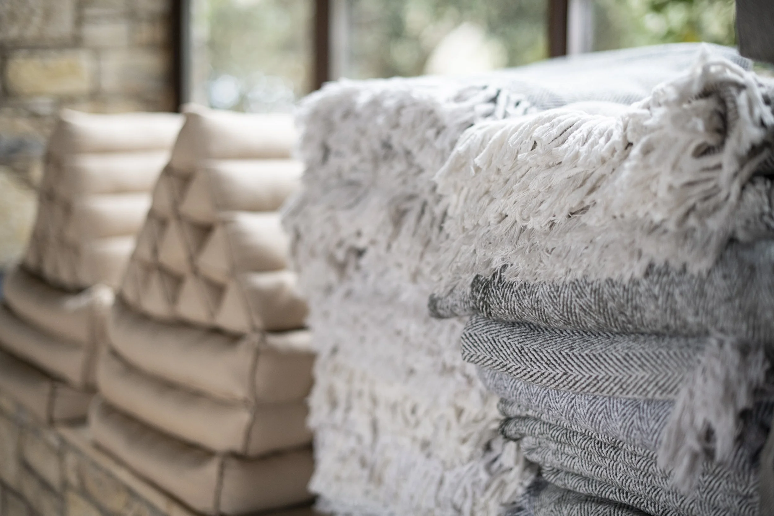 Stacked folded blankets and pillows on a table with a blurred background.