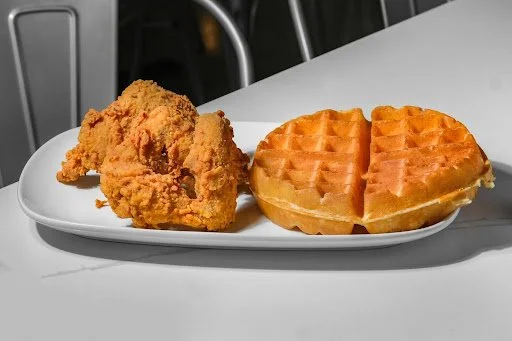 Fried chicken wing and two waffles on a white plate