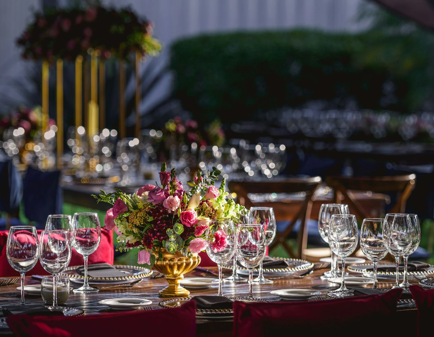 Elegant outdoor dining setup with a floral centerpiece, wine glasses, and tableware at a garden event.