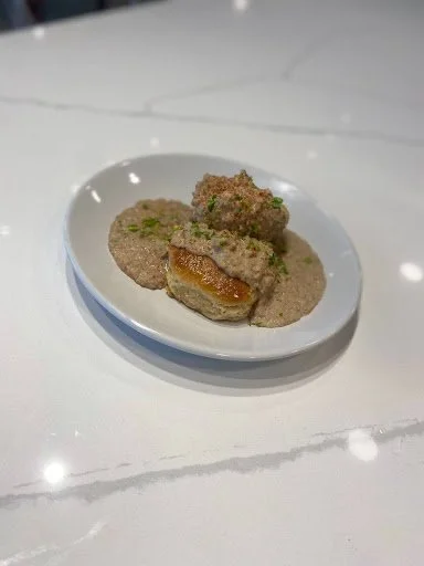 Fried food balls served on a white plate, one cut in half showing a filling inside, on a white marble table.