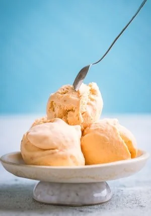 Three scoops of different flavored ice cream on a white plate with a spoon