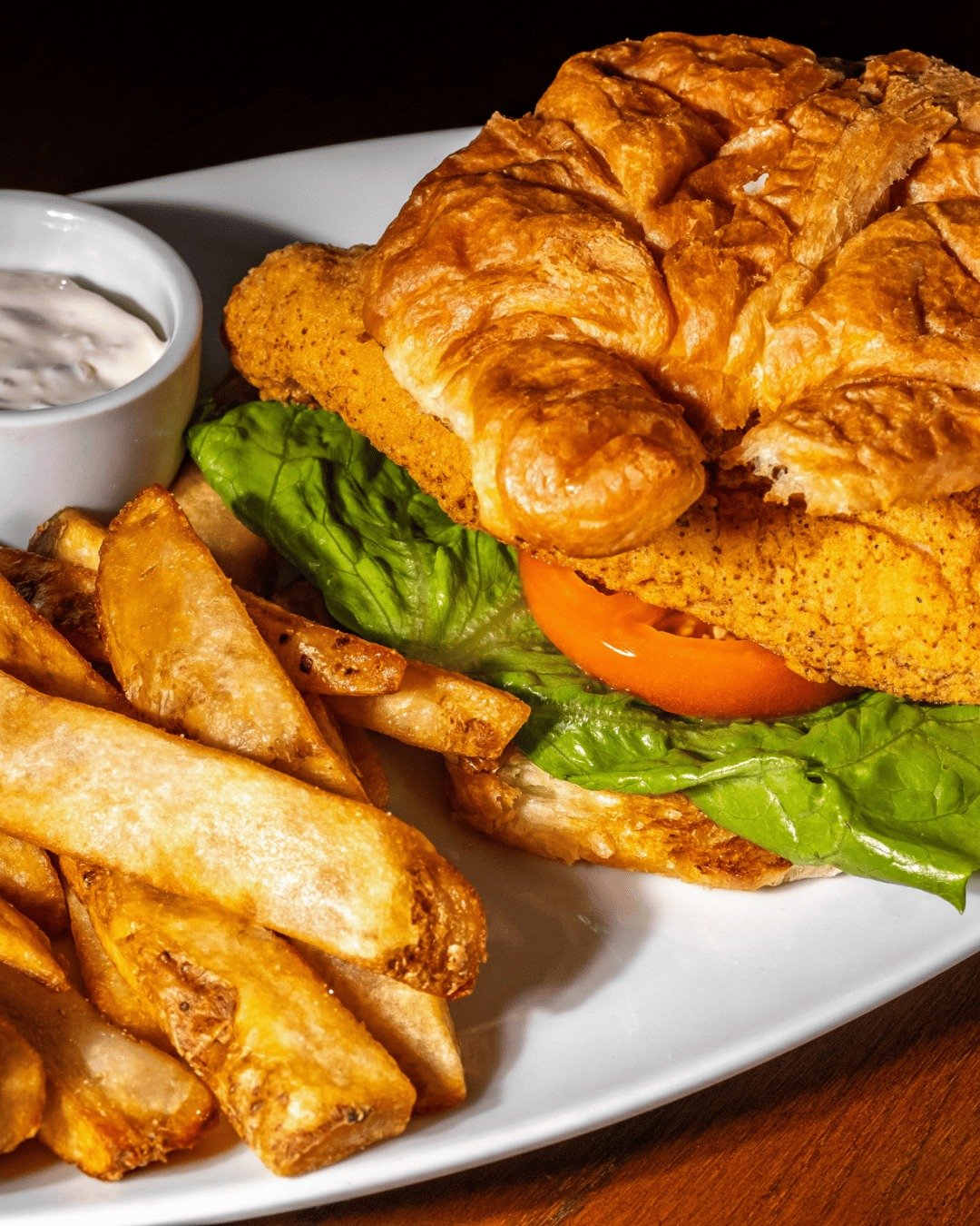 Fried fish sandwich with lettuce and tomato, served with French fries and a side of tartar sauce.