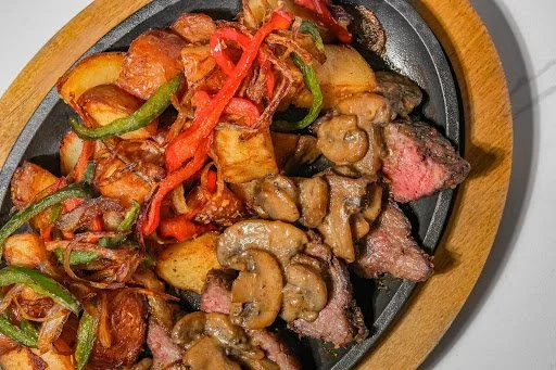 Cooked steak topped with sautéed mushrooms served with roasted potatoes and stir-fried vegetables.