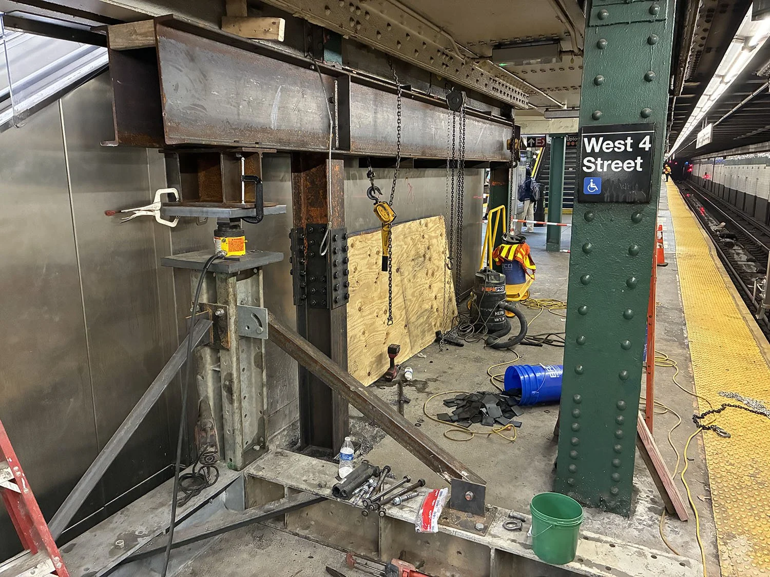 Construction work on a subway platform at West 4th Street station, with tools, equipment, and safety gear around, near the train tracks.