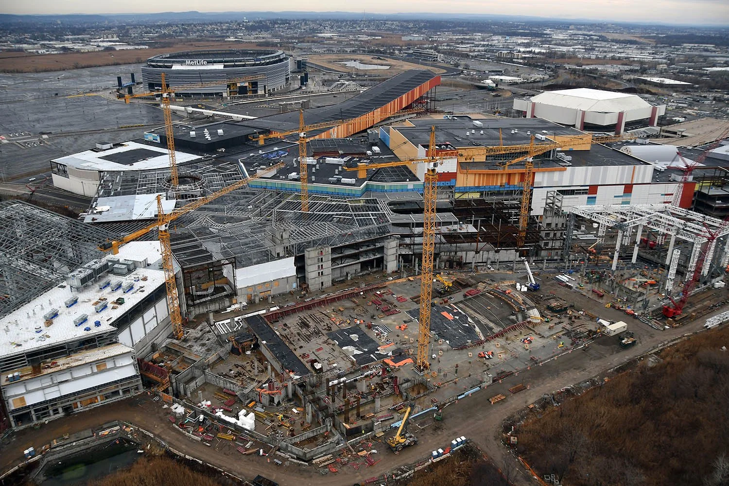 Aerial view of a construction site with multiple cranes building a large complex, with a stadium in the background.