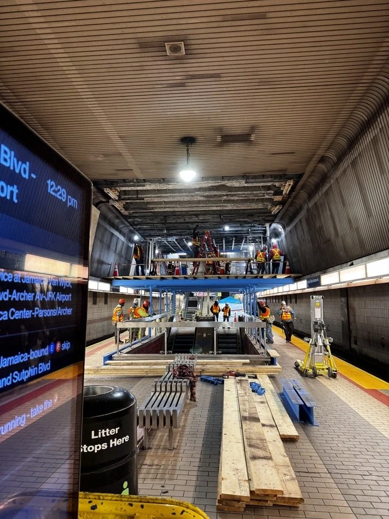 Construction workers in safety gear working on ceiling repairs in a subway station with scaffolding and construction materials.