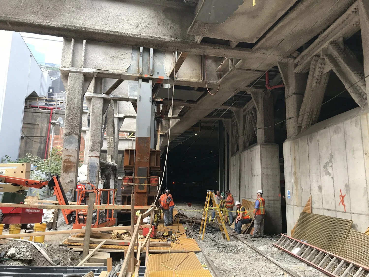 Construction workers in safety vests and helmets working on a large building site with concrete and steel structures.