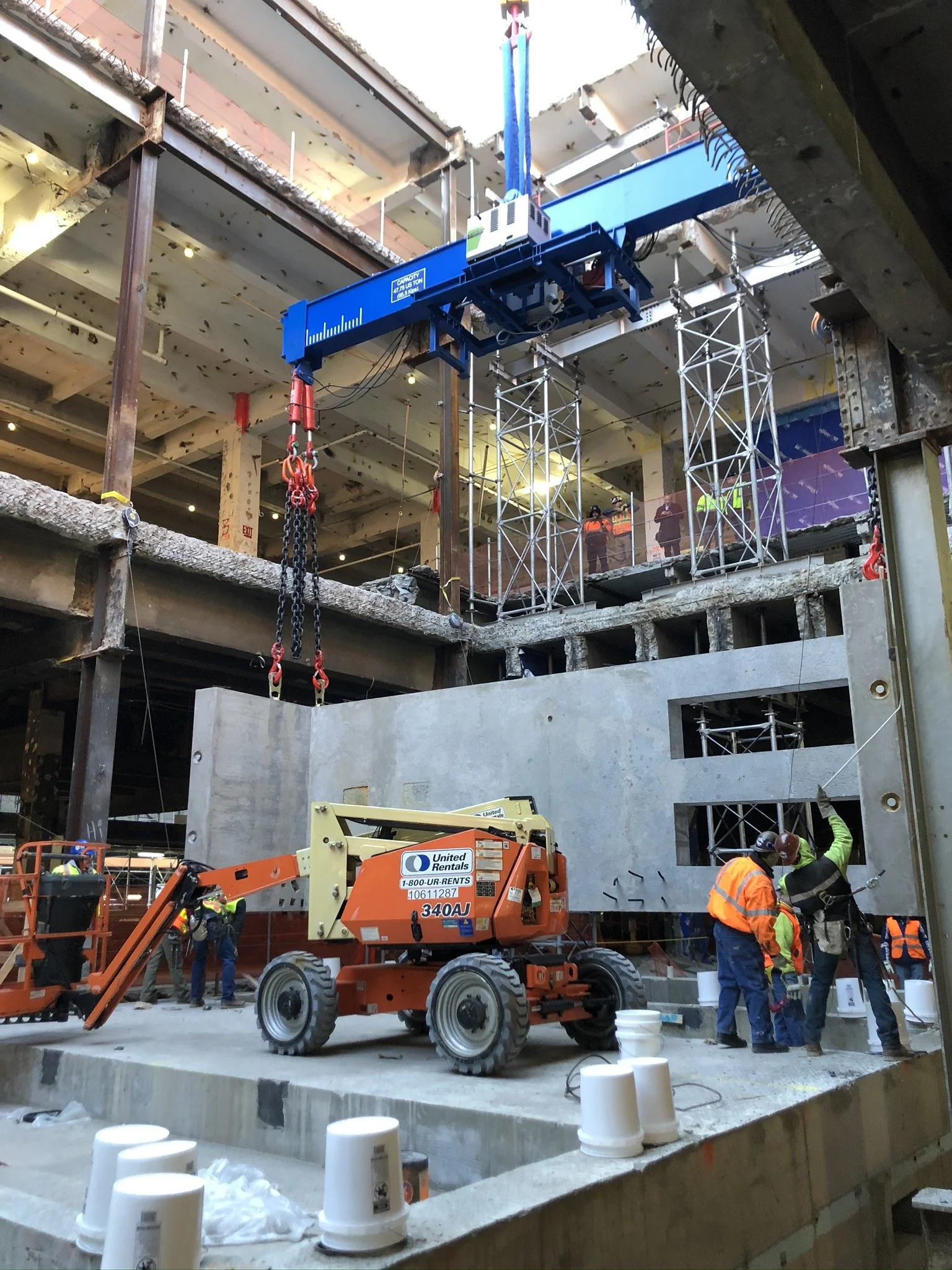 Construction workers on site installing a large concrete wall, with heavy machinery and scaffolding present.