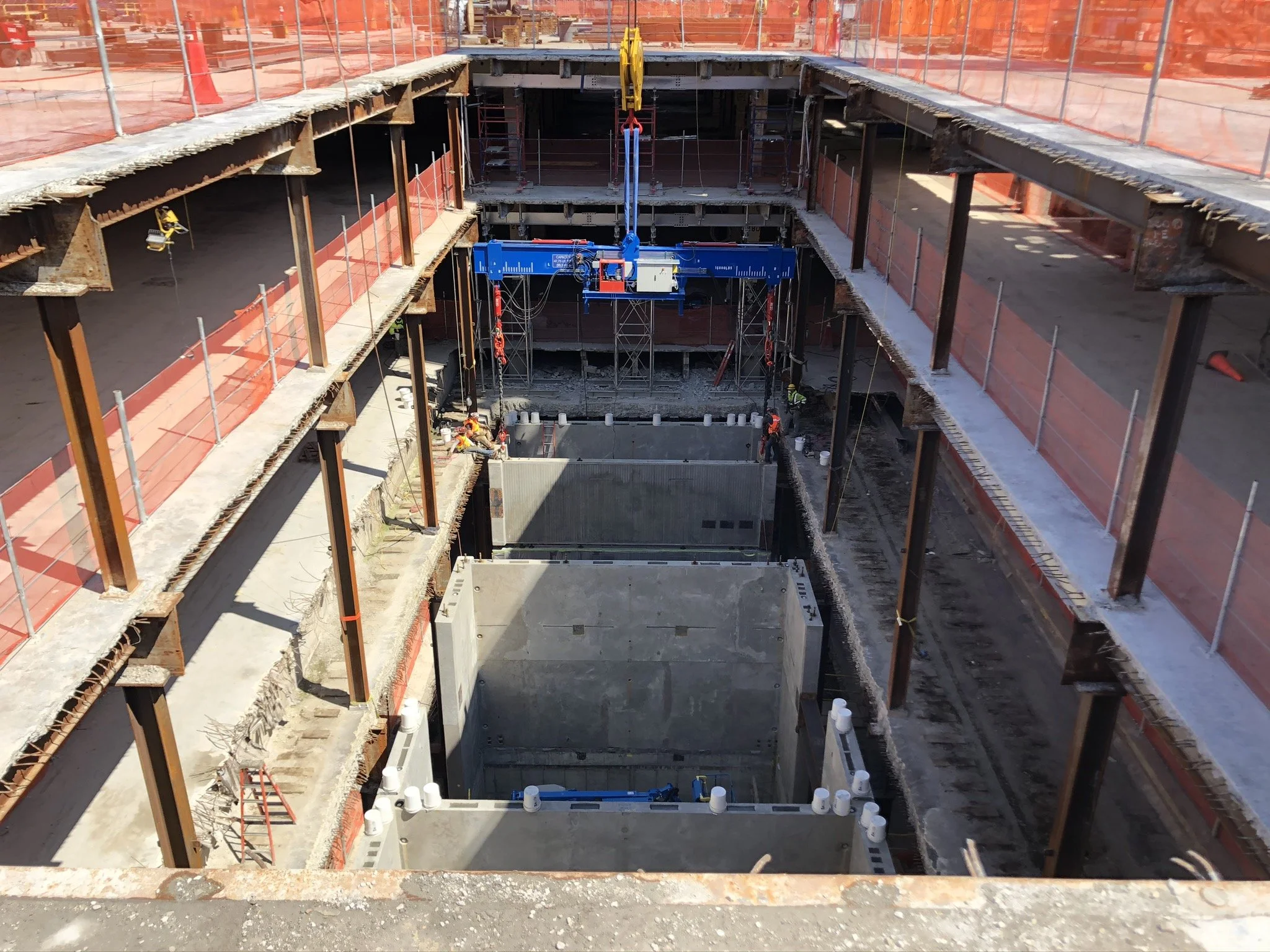 Construction site with excavation pits, steel beams, scaffolding, and workers installing concrete structures.