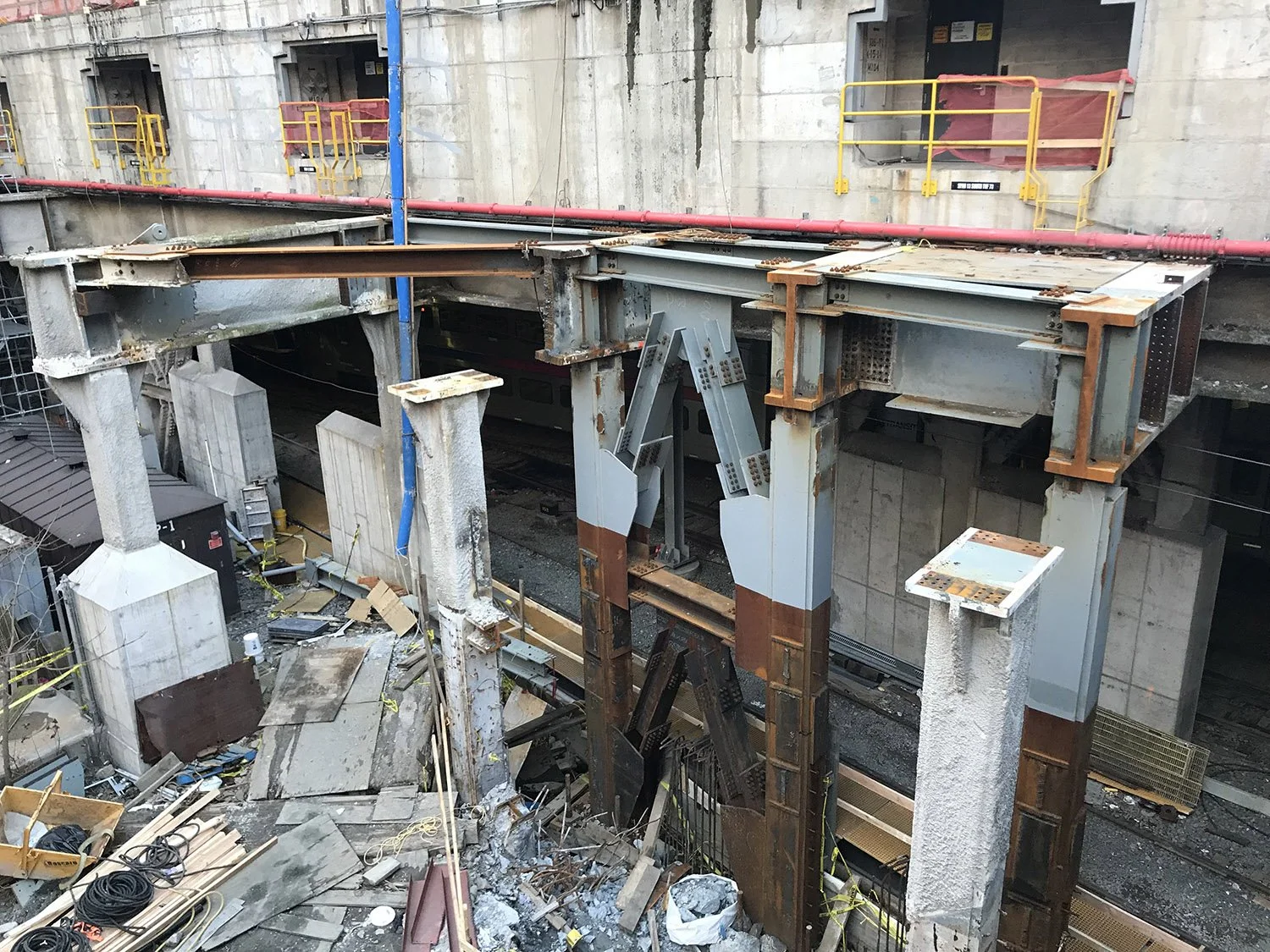Construction site with damaged columns and steel beams supporting a concrete structure. Building appears incomplete or under renovation.