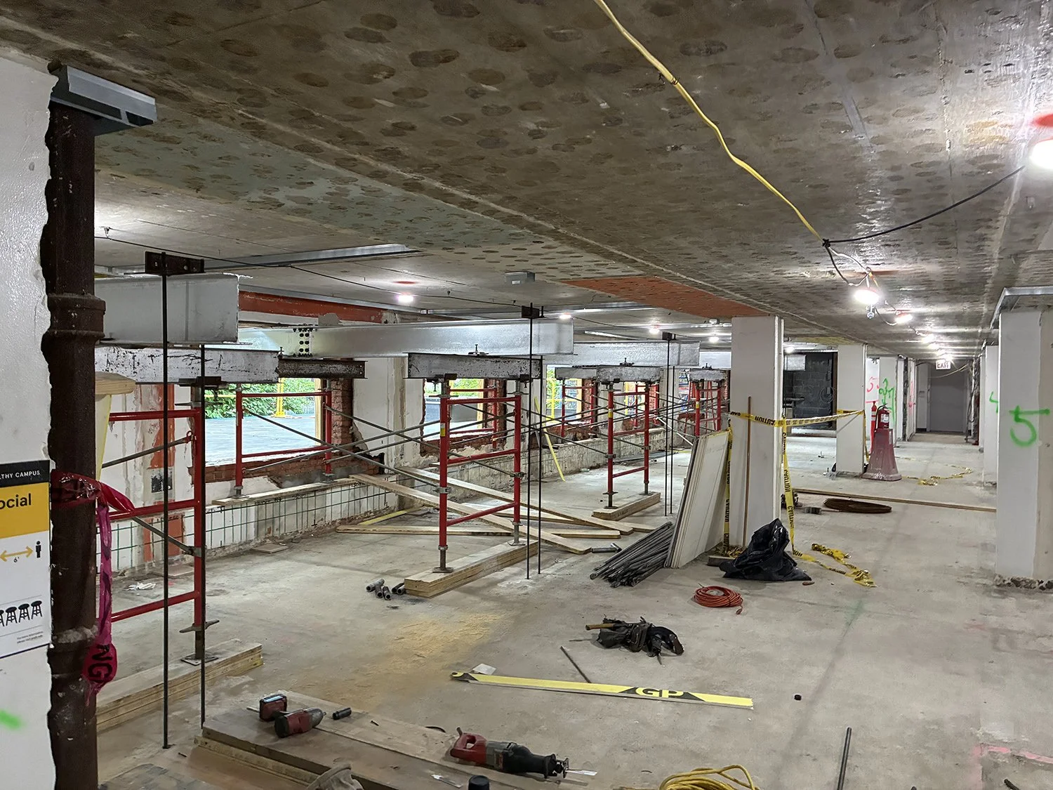 Construction site with exposed pipes, scaffolding, and construction materials inside a building.