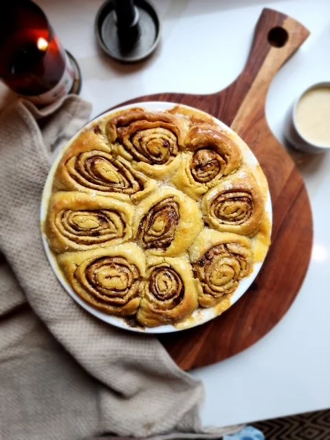 cinnamon rolls sitting on a cutting board with a tea towel next to it on the counter