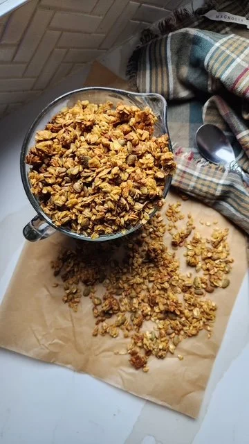granola with pumpkin seeds sitting on the counter on parchment paper spilling out of a large glass measuring cup