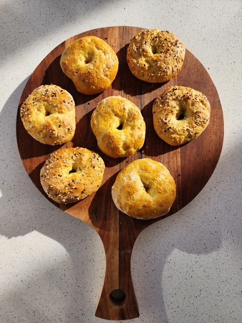 homemade bagels sitting on a cutting board on the counter in the sun