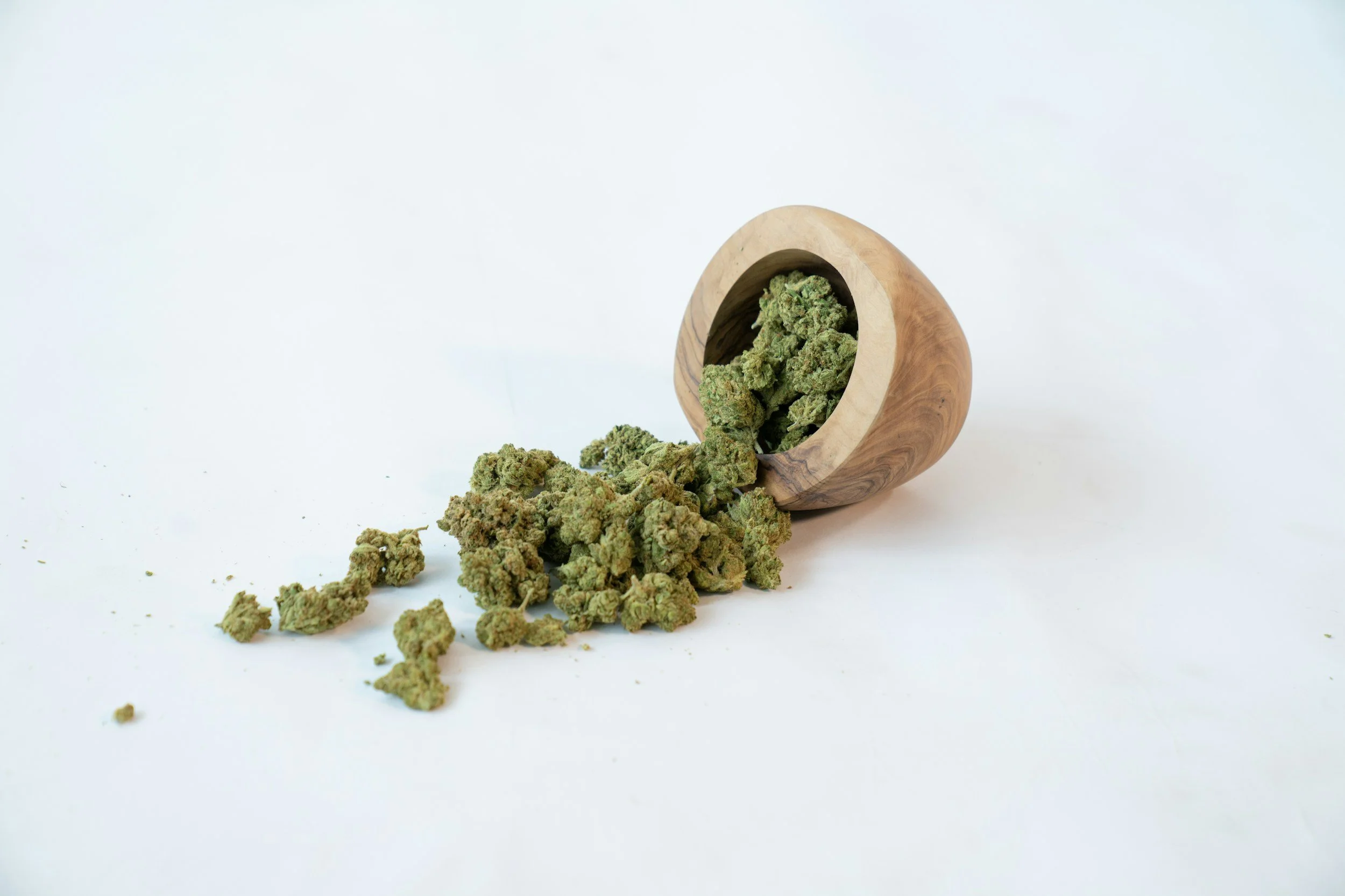 Cannabis buds spilling from a wooden bowl onto a white surface.