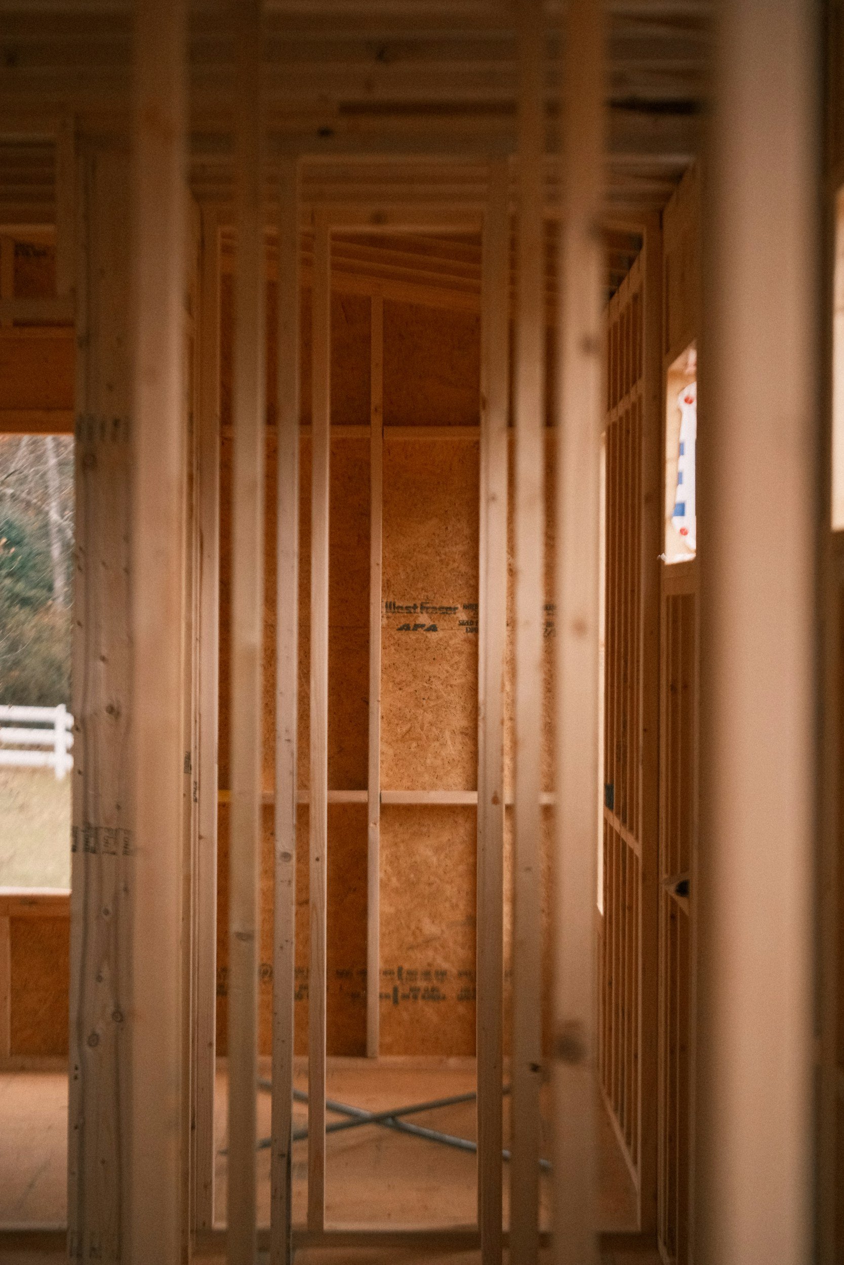 Interior view of a wooden framed structure under construction, showing vertical studs and plywood sheathing.