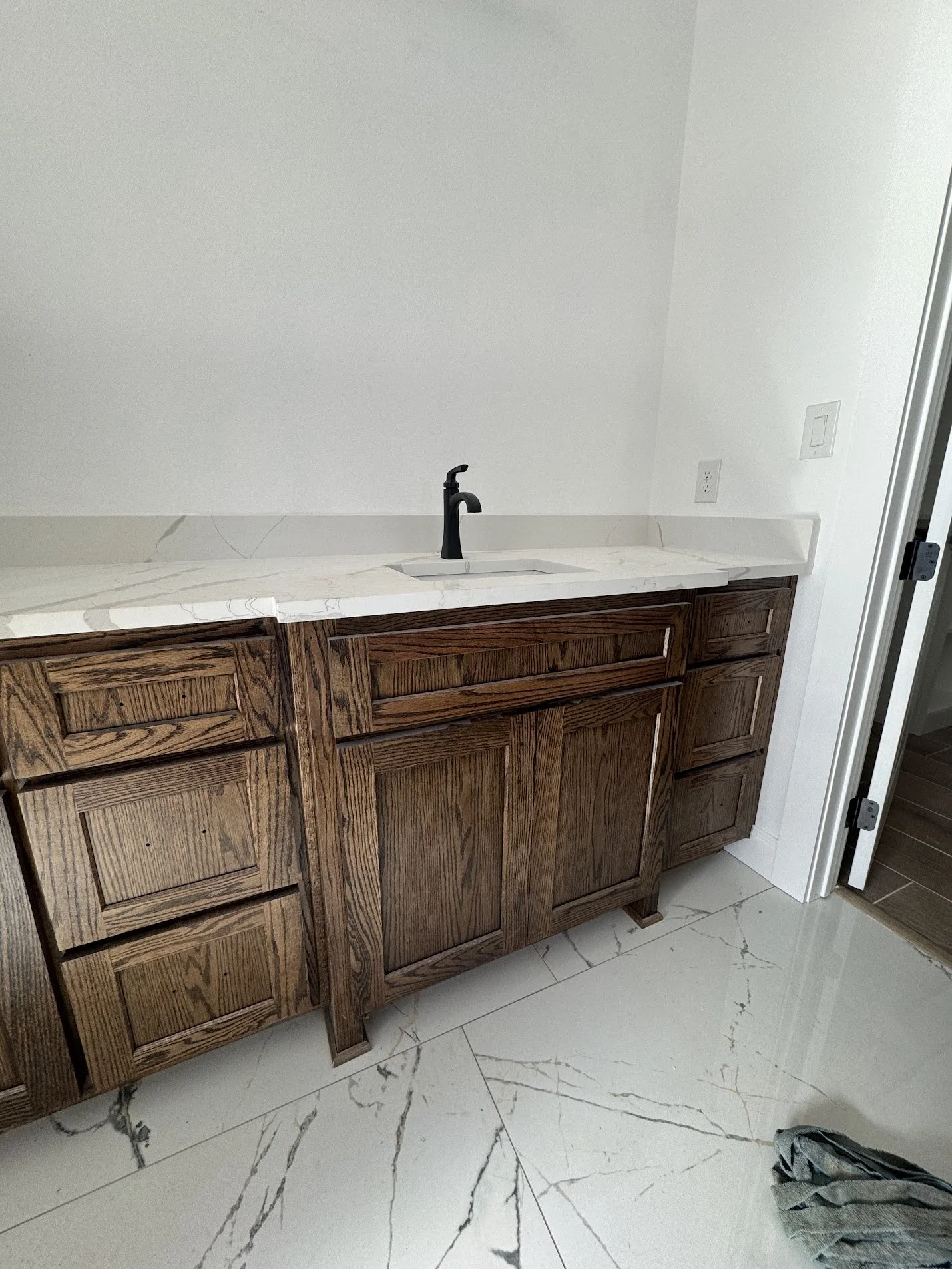 Kitchen with wooden cabinets, marble countertop, black faucet, and a white wall in the background.