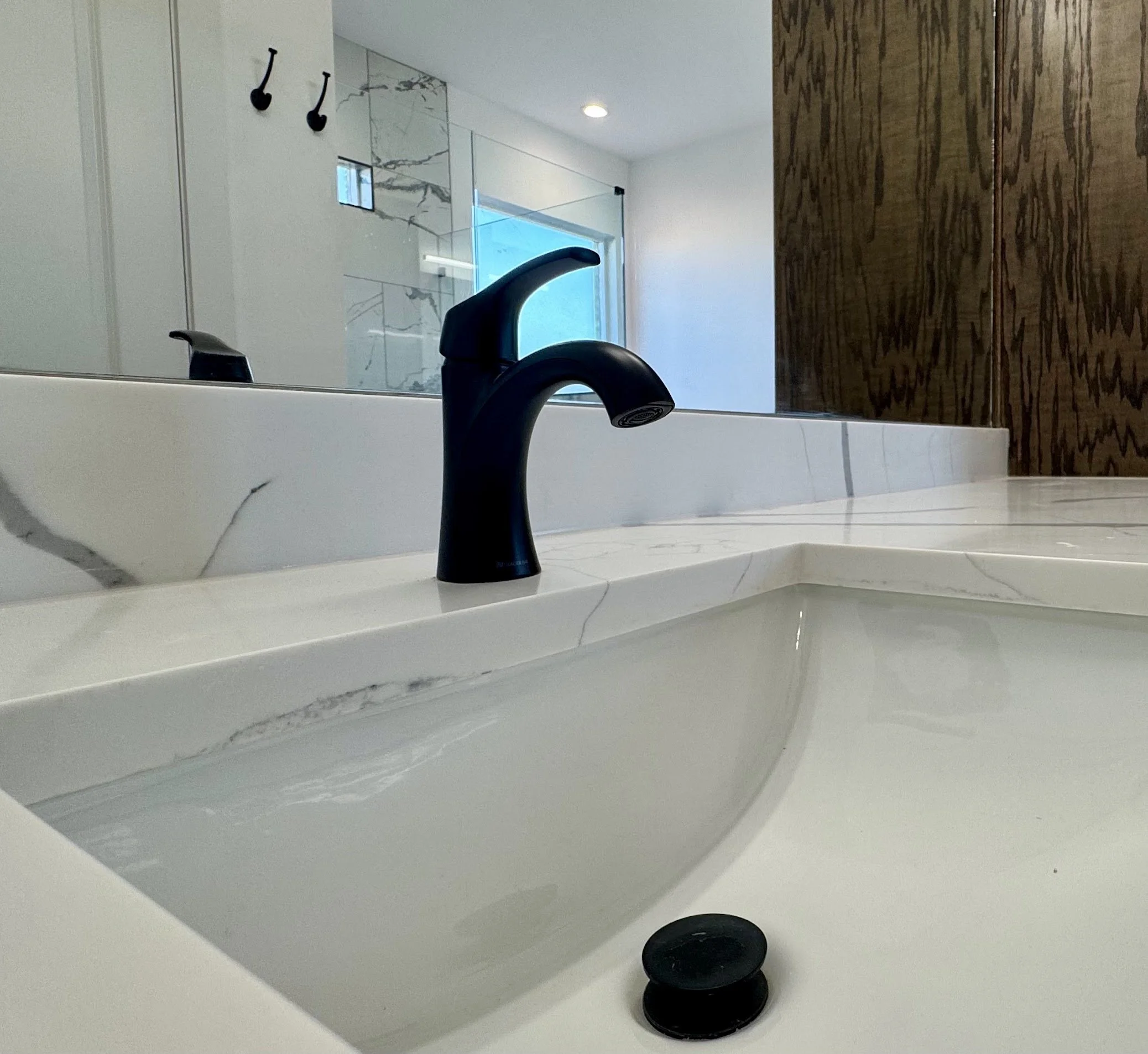 Close-up of a black faucet on a white marble bathroom sink with a blurred mirror and shower area in the background.
