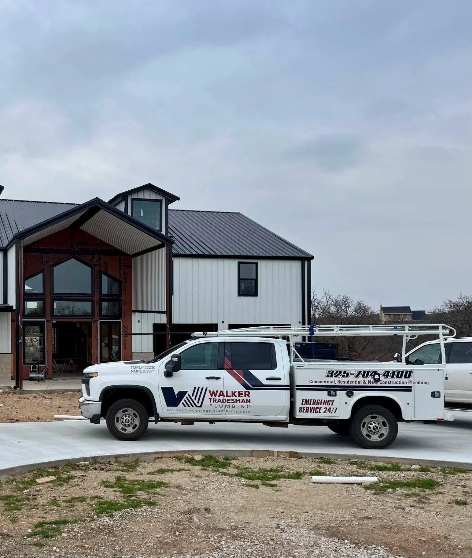 A construction company truck parked in front of a house under construction, with a modern two-story house with black and white exterior and large windows in the background.