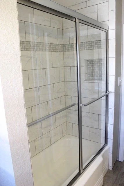 Glass shower enclosure with beige and gray tiled walls and a built-in niche.