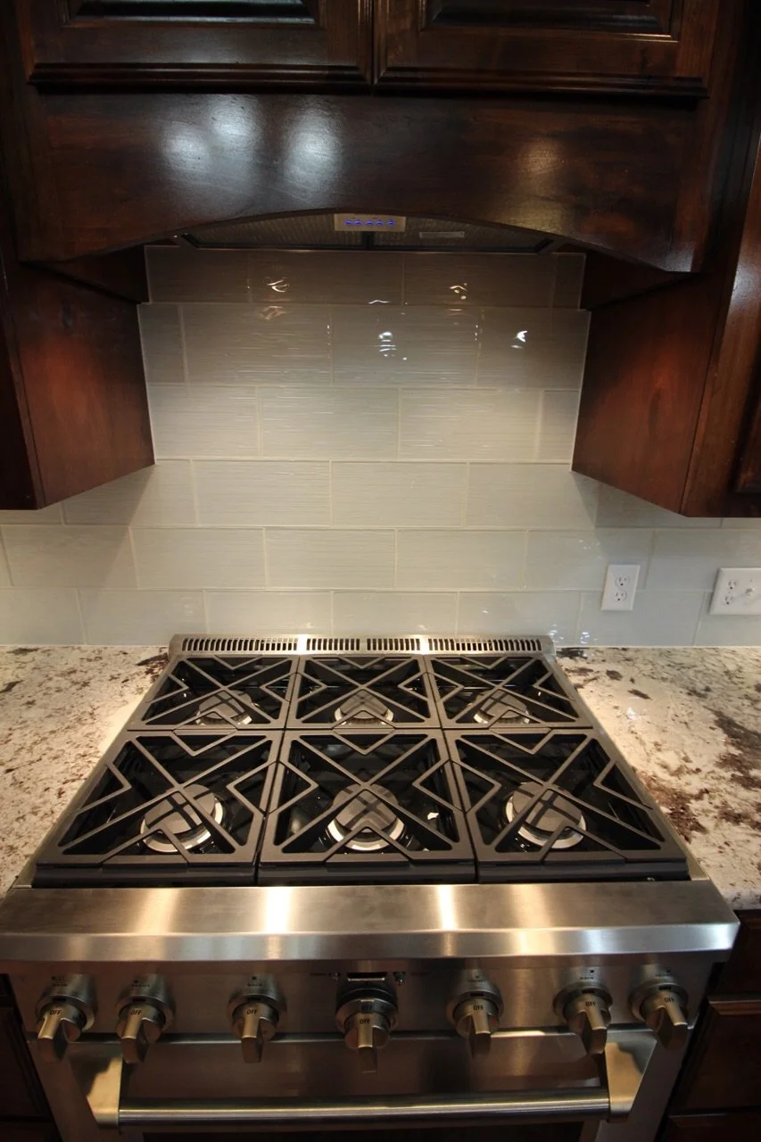 Kitchen stove with six burners and dark wood cabinets above, cream-colored tile backsplash, and granite countertop.