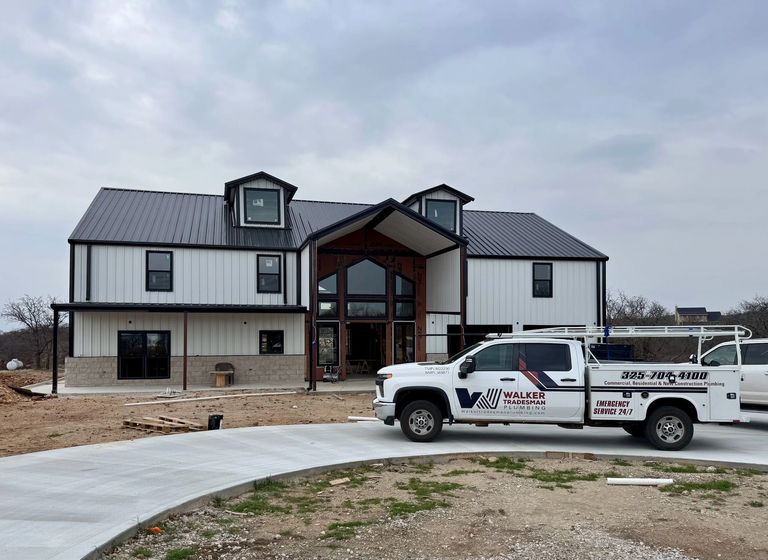 New construction house with black roof and white siding, work truck parked in front, and ongoing building activity.