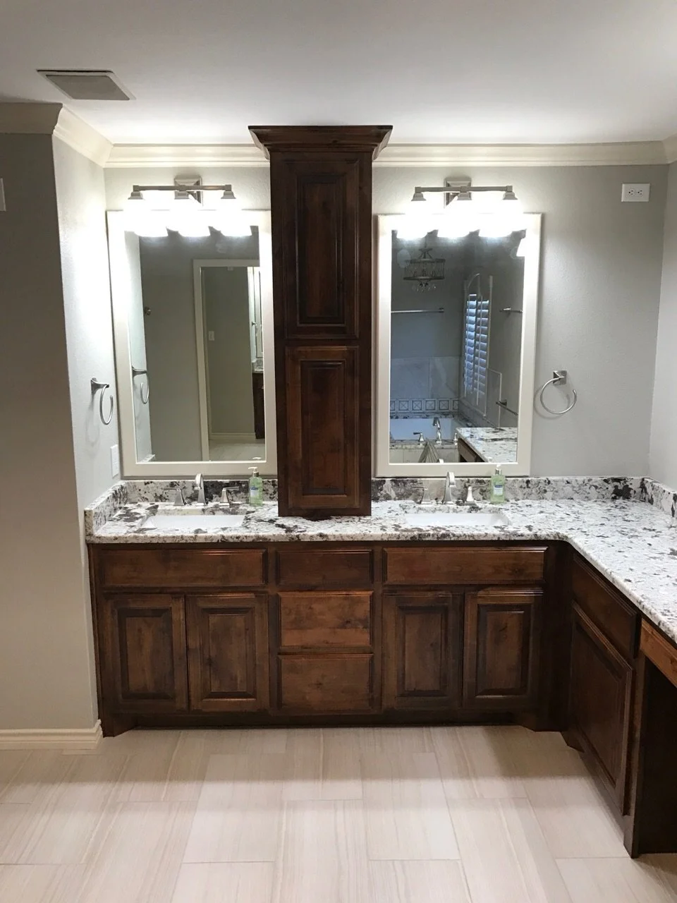 Bathroom vanity with dual mirrors, granite countertops, and wooden cabinets, view of a bathtub and shower through the mirrors.