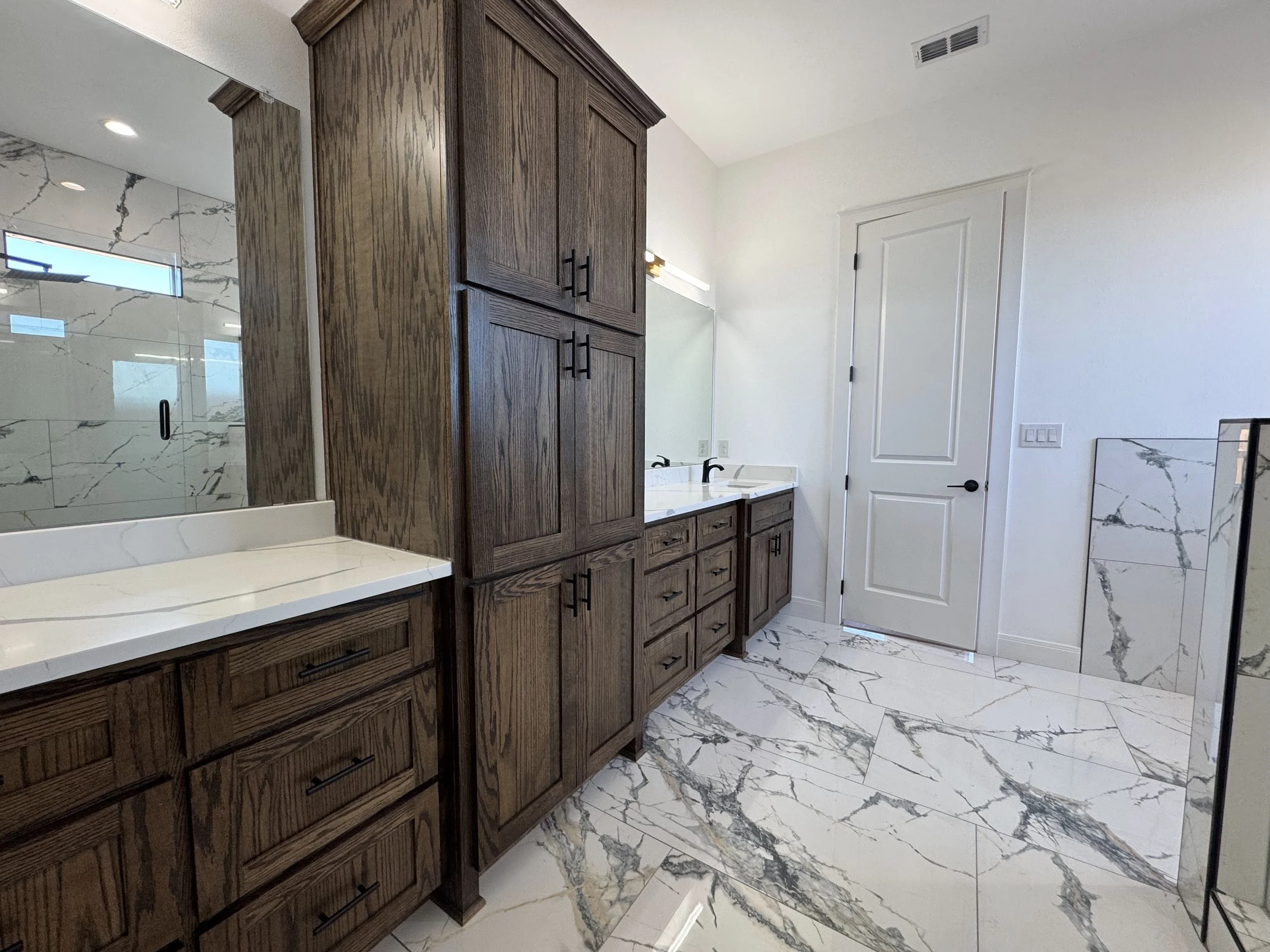 Bathroom with wooden cabinets, white marble countertops, and a walk-in shower with marble tiles and a glass door.