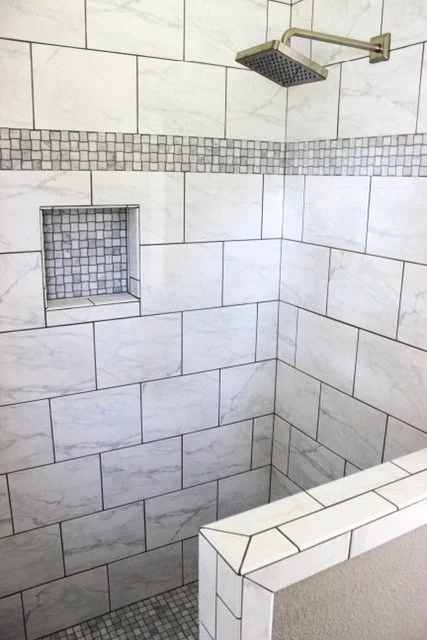 A modern shower with white marble tiles, a built-in niche with small gray tiles, and a rain shower head.