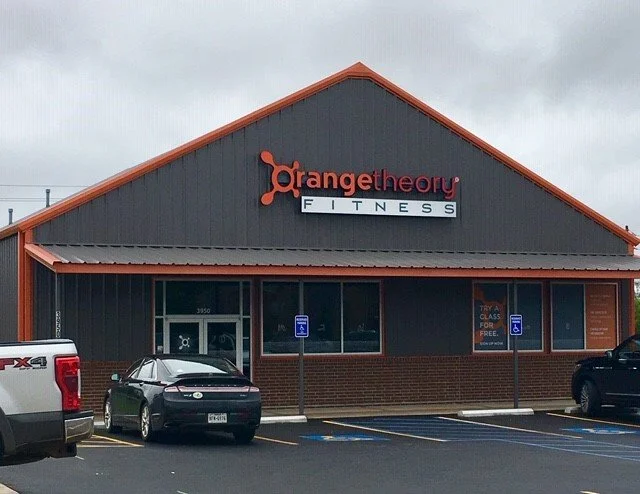 Front of a fitness center named Orange Theory Fitness with parking spaces and cars in front.
