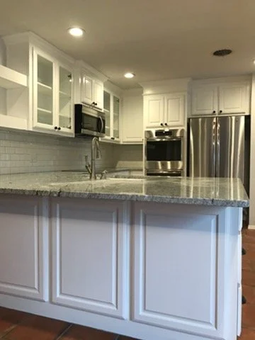 Modern kitchen with white cabinets, stainless steel refrigerator, oven, microwave, and granite countertop