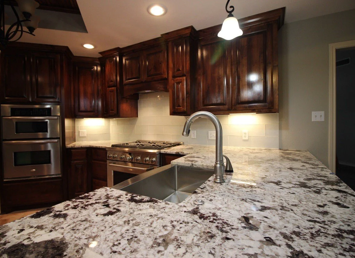 Kitchen with dark wooden cabinets, granite countertops, stainless steel oven and stove, and a sink with a modern faucet.