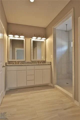 Bathroom with dual mirrors, vanity with granite countertop, and a walk-in shower with glass door.