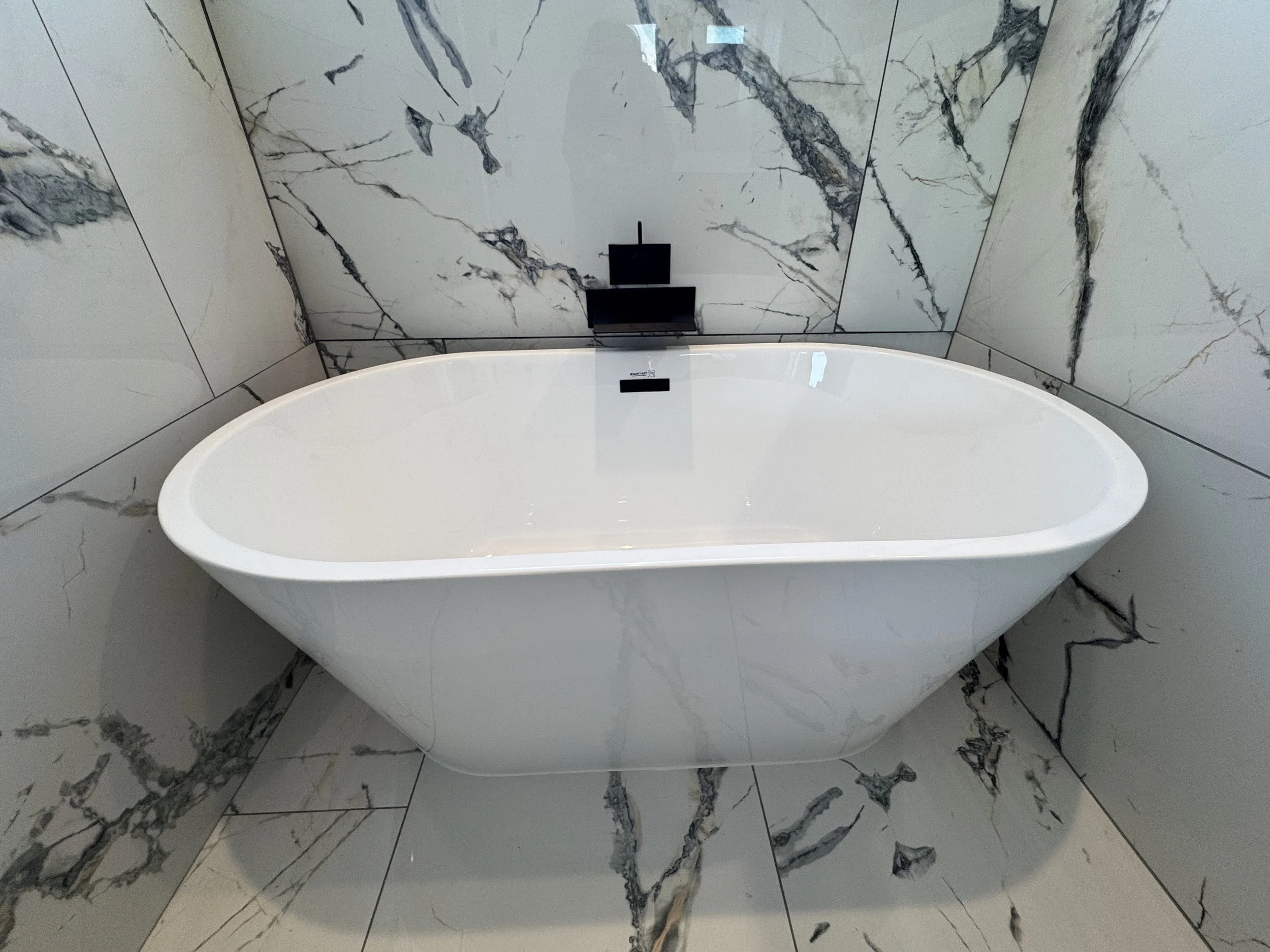 A modern white bathtub positioned against marble tiled walls in a bathroom.