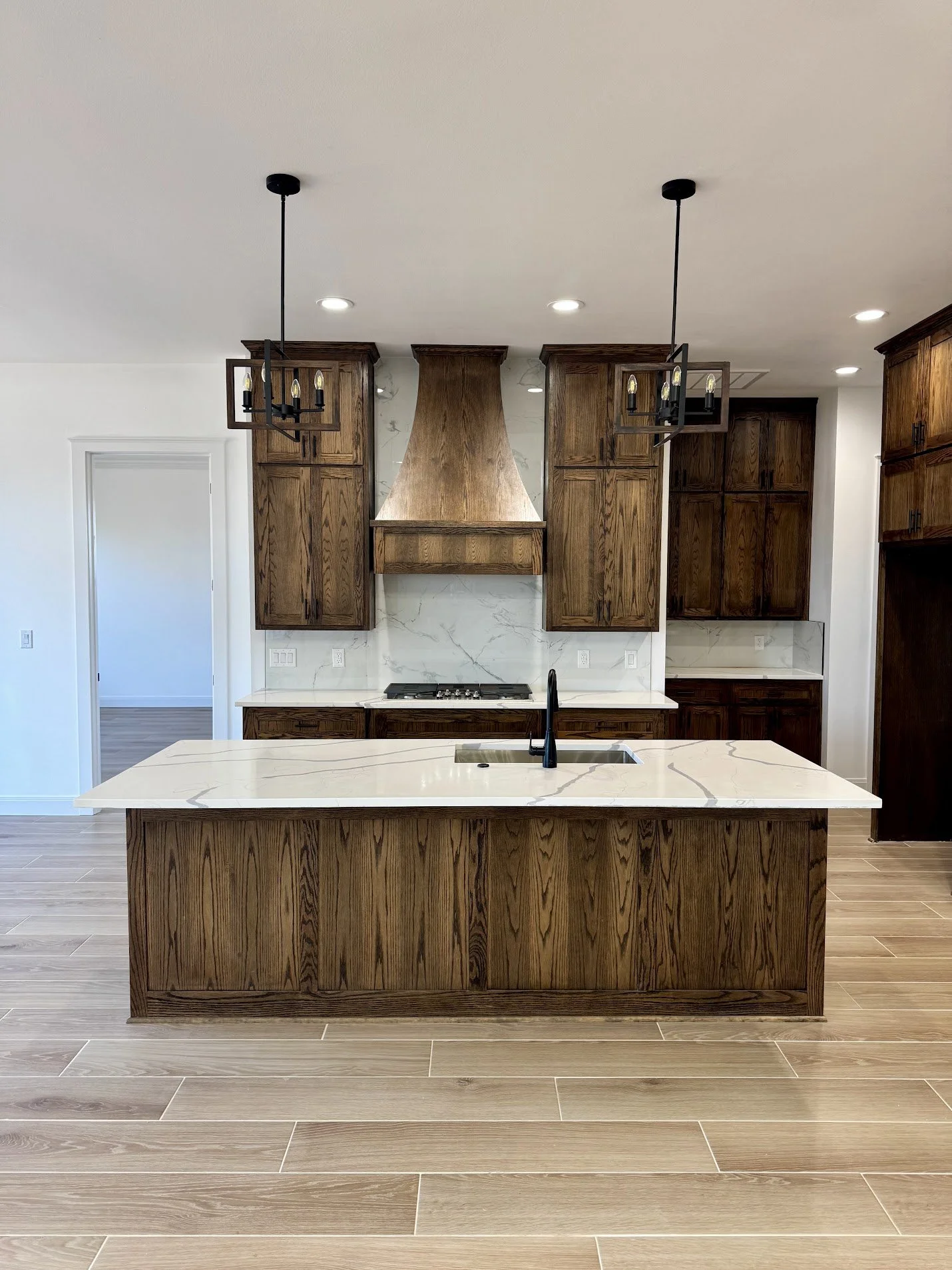 Modern kitchen with wooden cabinets, white marble countertops, an island with a sink, and black light fixtures