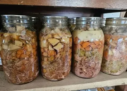 Four Mason jars filled with layered food items, including meats and vegetables, on a wooden shelf.