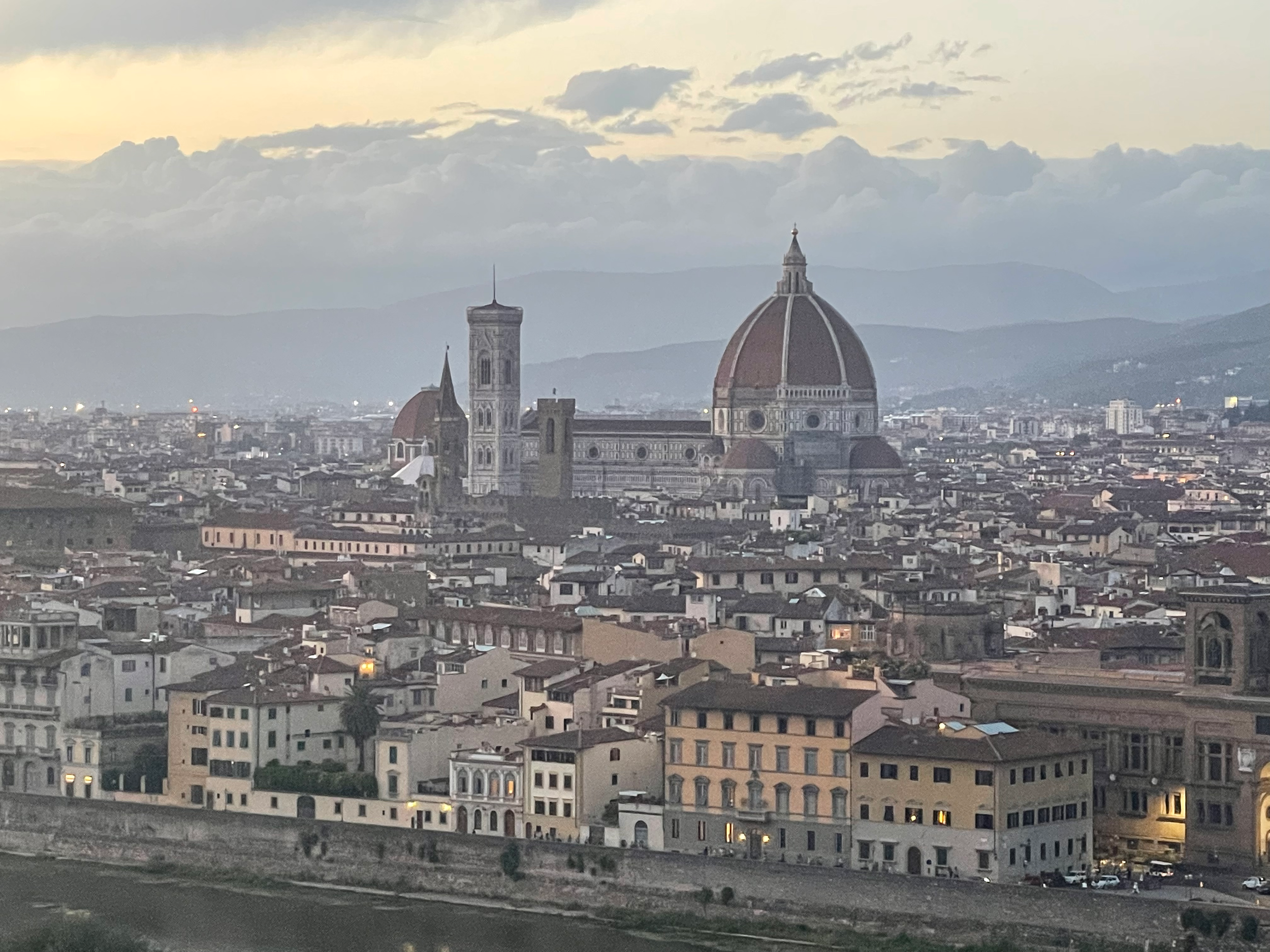 Cityscape of Florence, Italy with the Florence Cathedral's dome (Santa Maria del Fiore), alongside other historic buildings, under a cloudy sky.