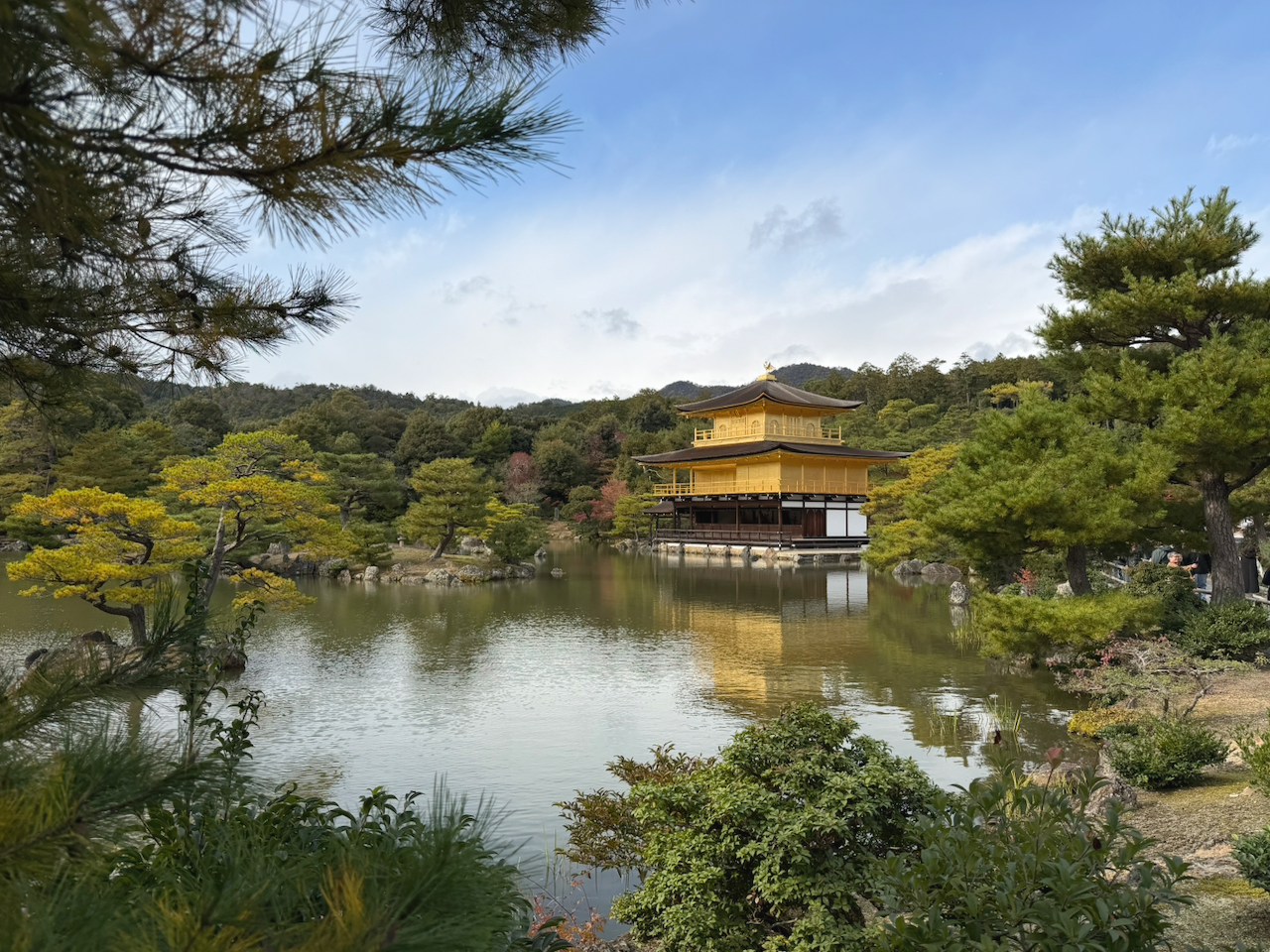 Traditional Japanese temple by a calm lake surrounded by lush green trees and mountains in the background.