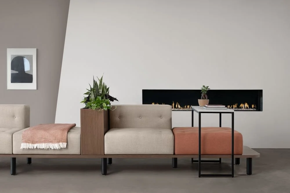 Modern living room with beige sectional sofa, potted plants, framed wall art, and a linear fireplace built into the plain wall.
