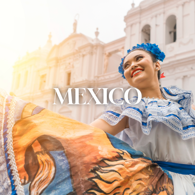 A smiling woman dressed in traditional Mexican attire, with a blue floral headpiece, holding a colorful Mexican flag or textile in front of a historic building with statues, during a sunny day in Mexico.