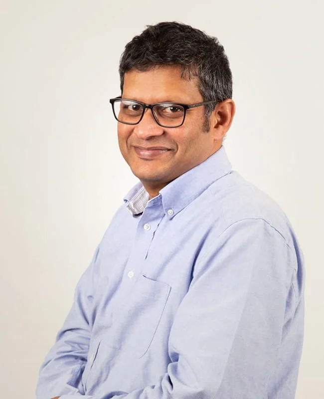Portrait of a man wearing glasses and a light blue button-up shirt against a plain background.