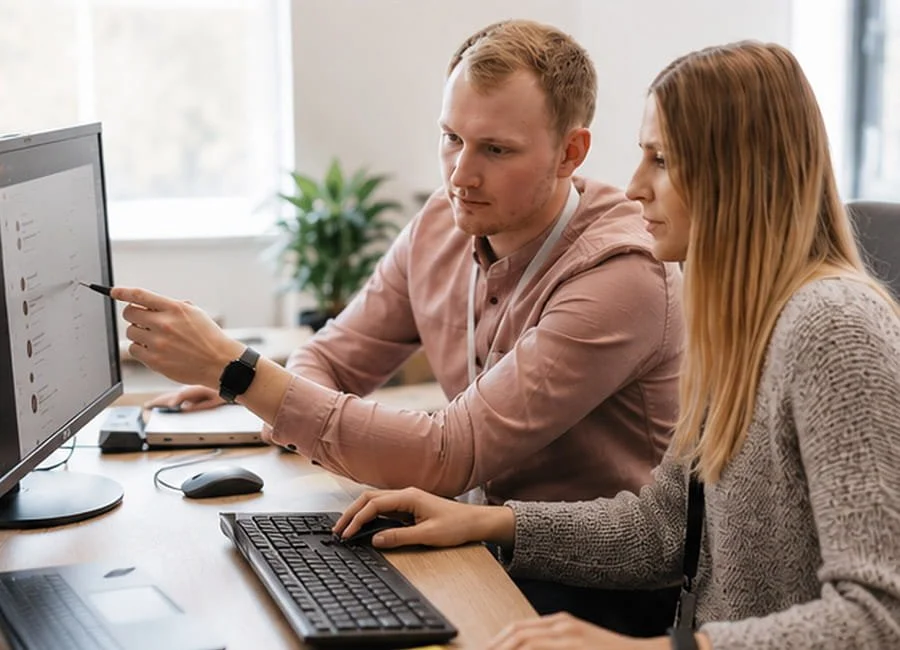 Two colleagues working together at a desk, discussing something on a computer screen.